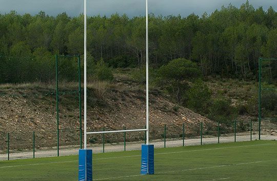Poteaux de but de rugby sur un terrain herbeux avec une colline boisée en arrière-plan