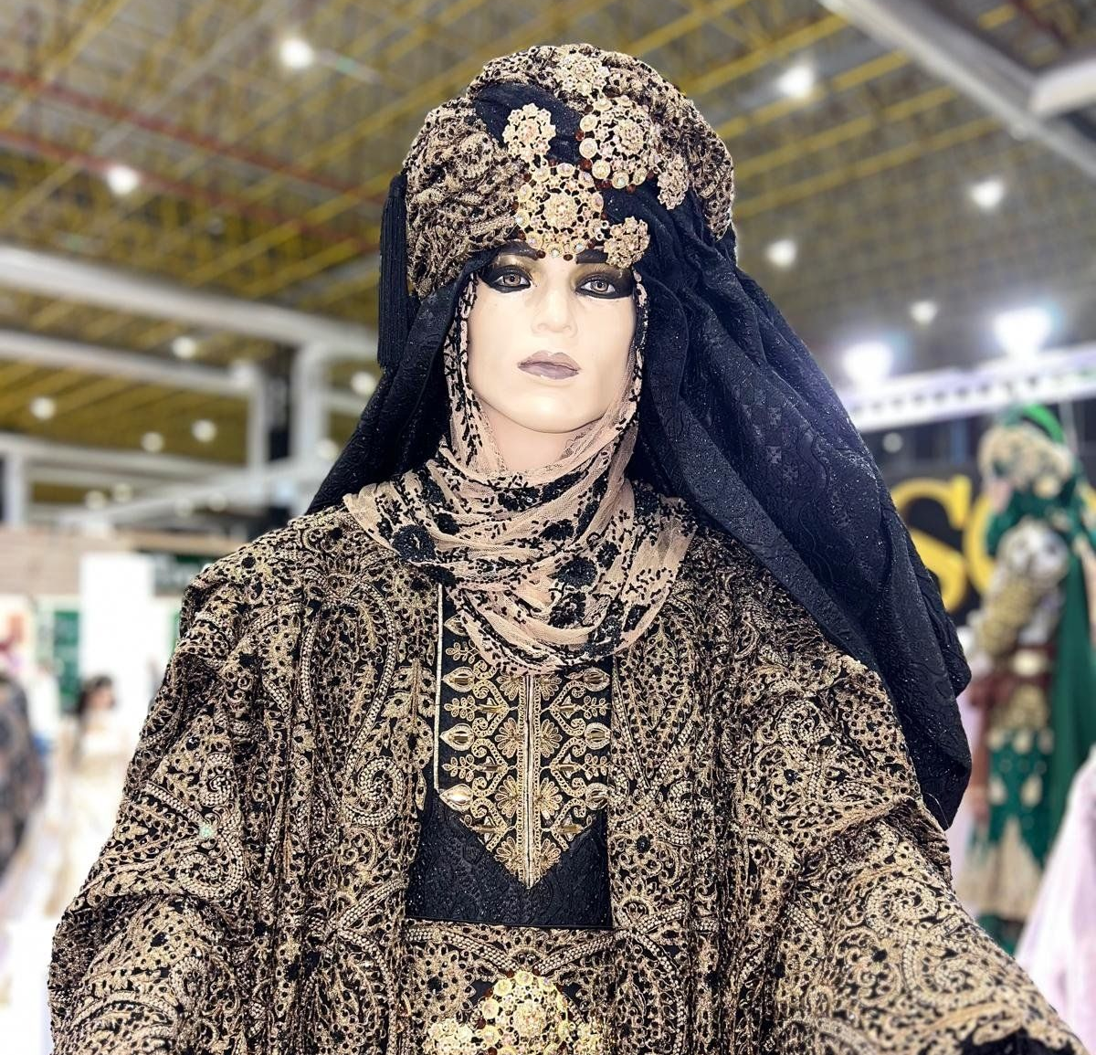 Maniquí con traje de Oriente Medio adornado en dorado y negro, con un gran tocado adornado con joyas.