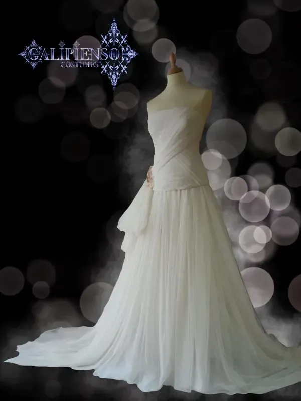 Vestido de novia blanco sin tirantes sobre maniquí; falda fluida, detalle de cinta, fondo bokeh oscuro.