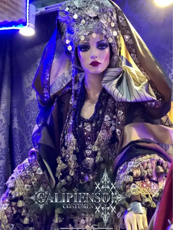 Maniquí con traje ornamentado con colores oscuros y tocado elaborado.