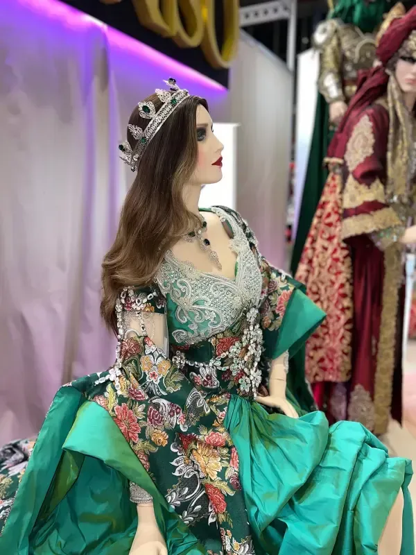 Maniquí con vestido verde y floral, tiara y joyas, con otro maniquí vestido al fondo.