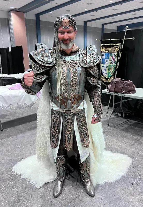 Persona con elaborada armadura plateada y casco con capa de piel blanca, posando con los puños cerrados.
