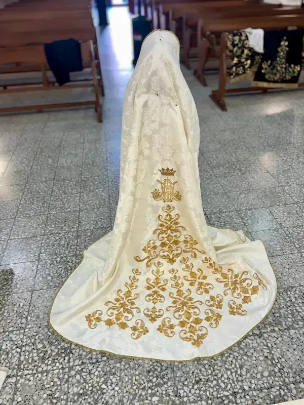 Una persona con una capa de color crema con bordados dorados, en una iglesia.