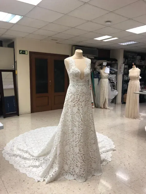 Un vestido de novia de encaje blanco sobre un maniquí con una larga cola, en una tienda de novias.