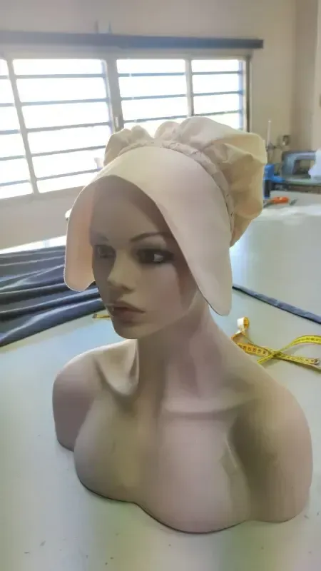 Cabeza de maniquí con sombrero de color claro con lazo, sobre una mesa cerca de una ventana.