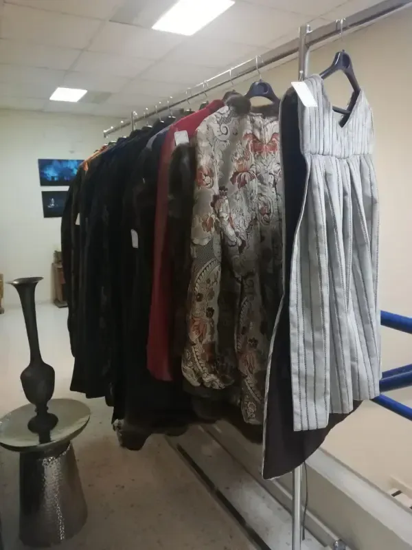 Perchero con diversas prendas, entre ellas chaquetas y un vestido de rayas, en el interior de una habitación.