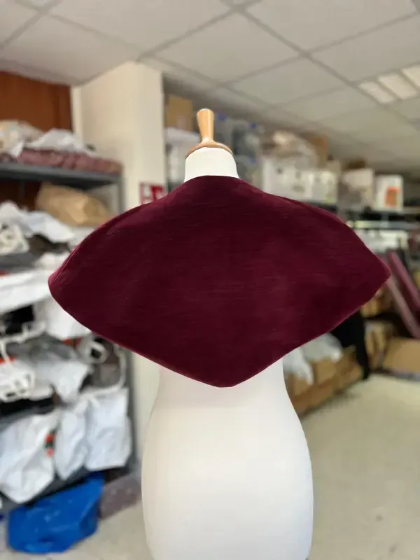 Capa burdeos colocada sobre un maniquí blanco en una tienda de telas.