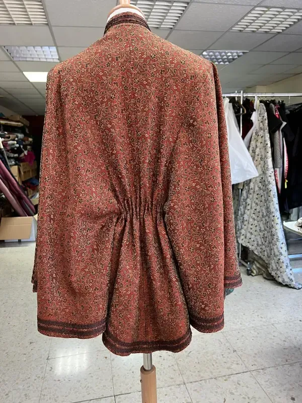 Vista posterior de un abrigo de color óxido con cintura ceñida sobre un maniquí, con ribete detallado.