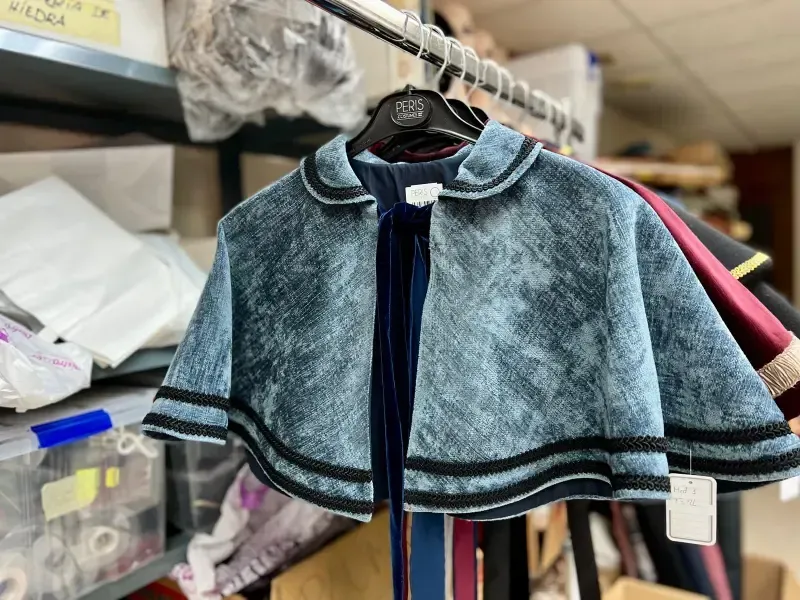 Capa de terciopelo azul con ribete negro colgada en un taller de costura.