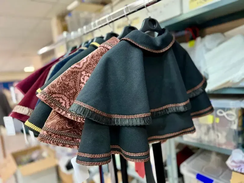 Varias capas de distintos colores y patrones cuelgan de un perchero, probablemente en un taller.