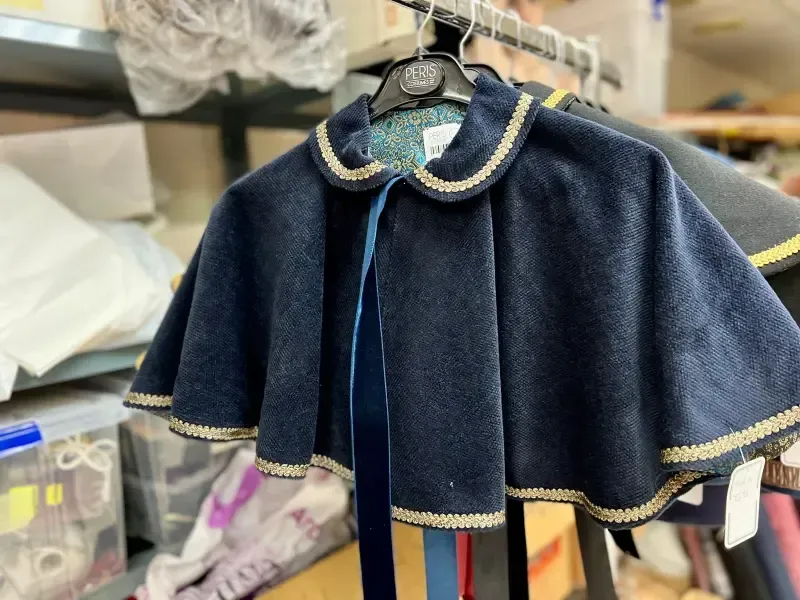 Capa azul oscuro con ribete dorado y lazo de cinta, colgada en un perchero.