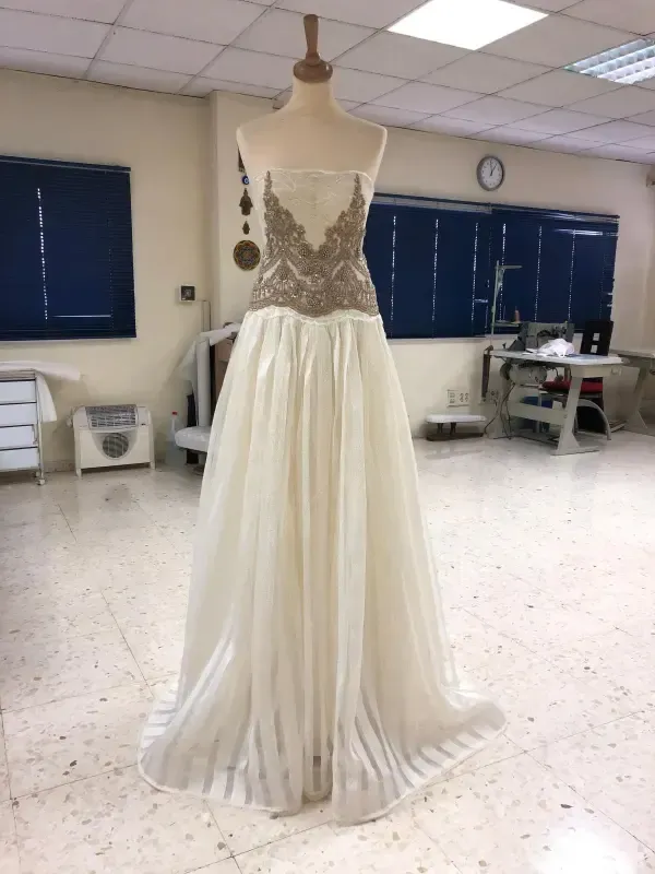 Vestido sin tirantes sobre maniquí con corpiño bordado en dorado y falda fluida de color crema en un estudio.