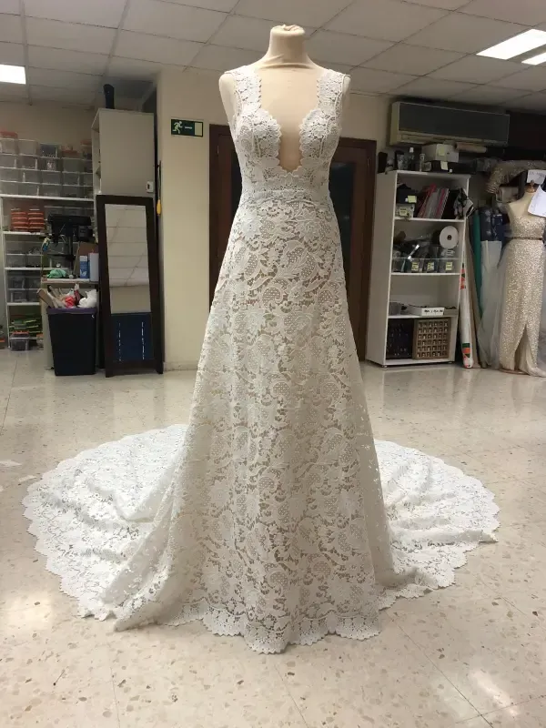 Vestido de novia de encaje blanco sobre maniquí, con escote pronunciado y larga cola, en una tienda.