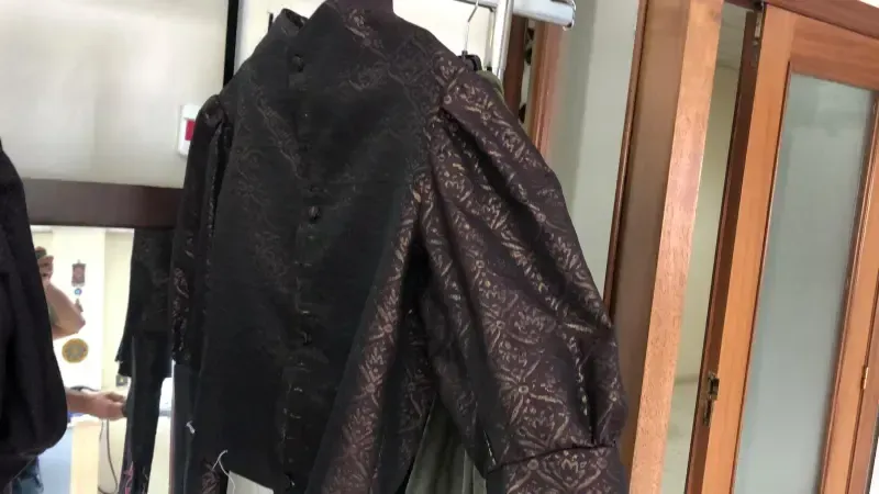 Camisa de manga larga con estampado metálico negro colgada en un perchero cerca de una ventana.