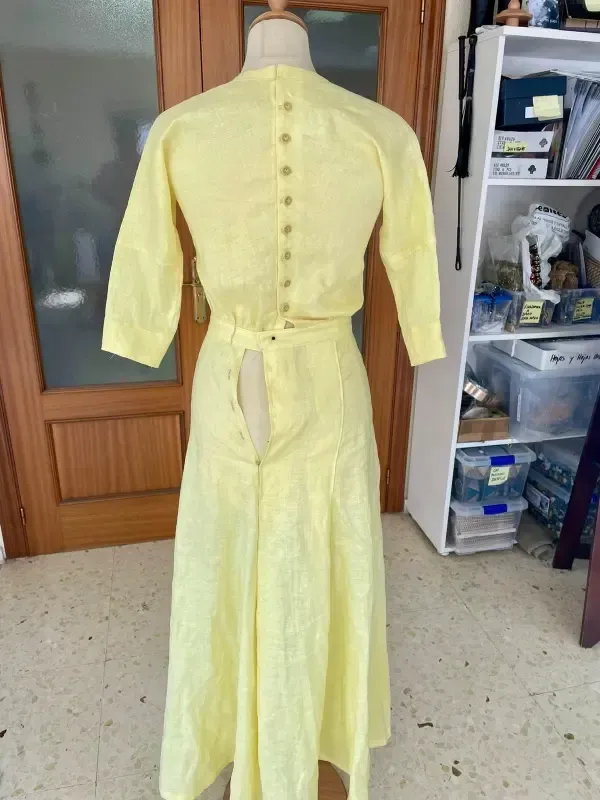 Vestido amarillo sobre maniquí, vista posterior, con botones y falda abierta, en el interior.