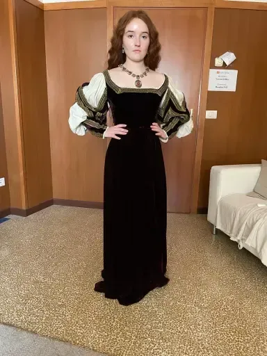 Mujer con un vestido de terciopelo con mangas abullonadas y collar de joyas, posando en el interior.