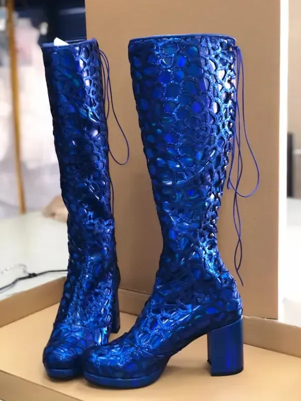 Par de botas altas, azules y brillantes, con tacones de bloque y cordones en la parte trasera.