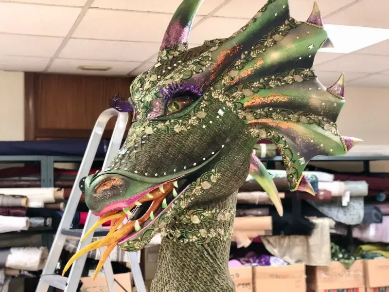 Una colorida escultura de cabeza de dragón con detalles en verde, morado y dorado; en un taller.