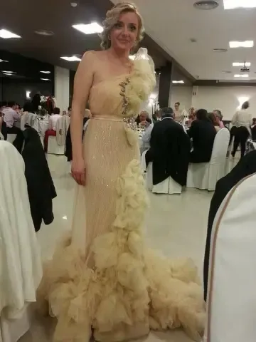 Mujer con un vestido formal de un solo hombro con detalles con volantes en un evento sentado.
