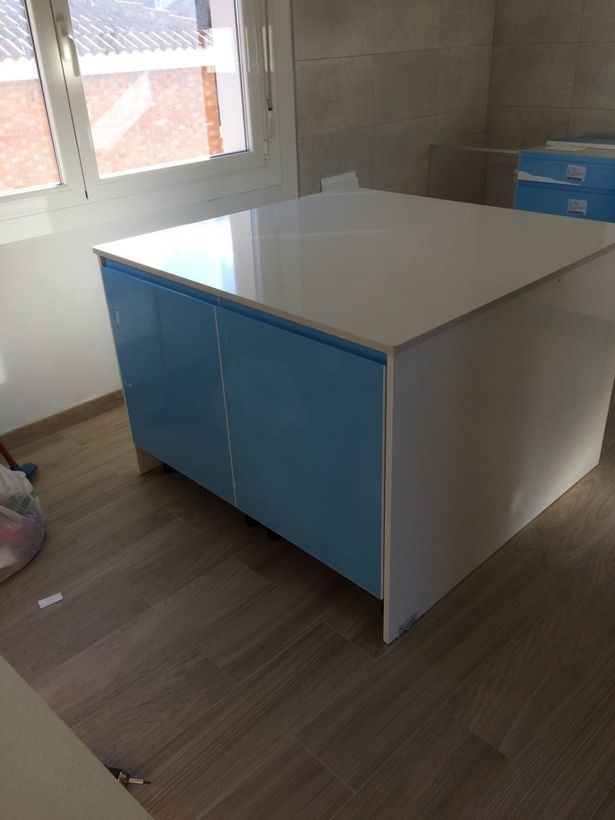 Una isla de cocina cuadrada con encimera blanca habitación con suelo que imita la madera.