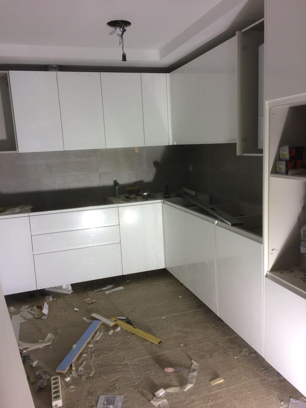 Una cocina blanca en forma de L durante su renovación, con escombros de construcción en el suelo y accesorios sin terminar.