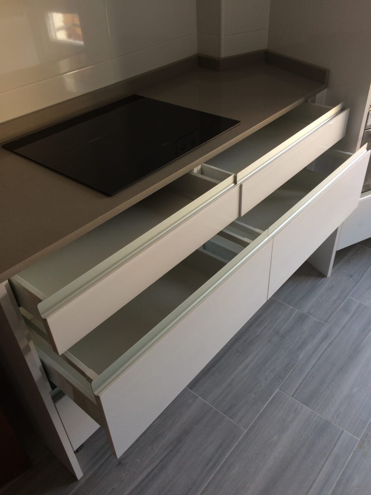 Una isla de cocina con placa de inducción y dos cajones abiertos de color claro sobre un suelo de baldosas grises.