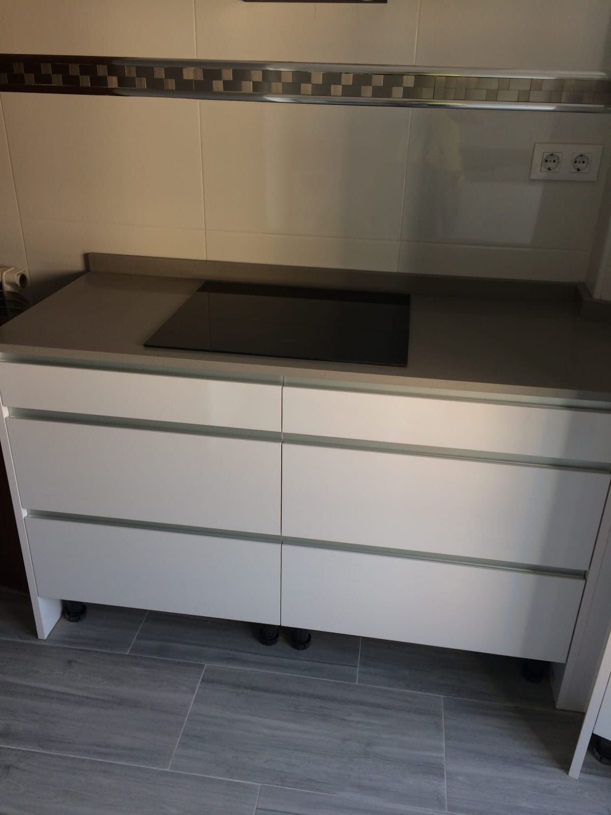 Mueble bajo de cocina moderno con encimera gris oscuro, placa de inducción negra integrada y cajones blancos.