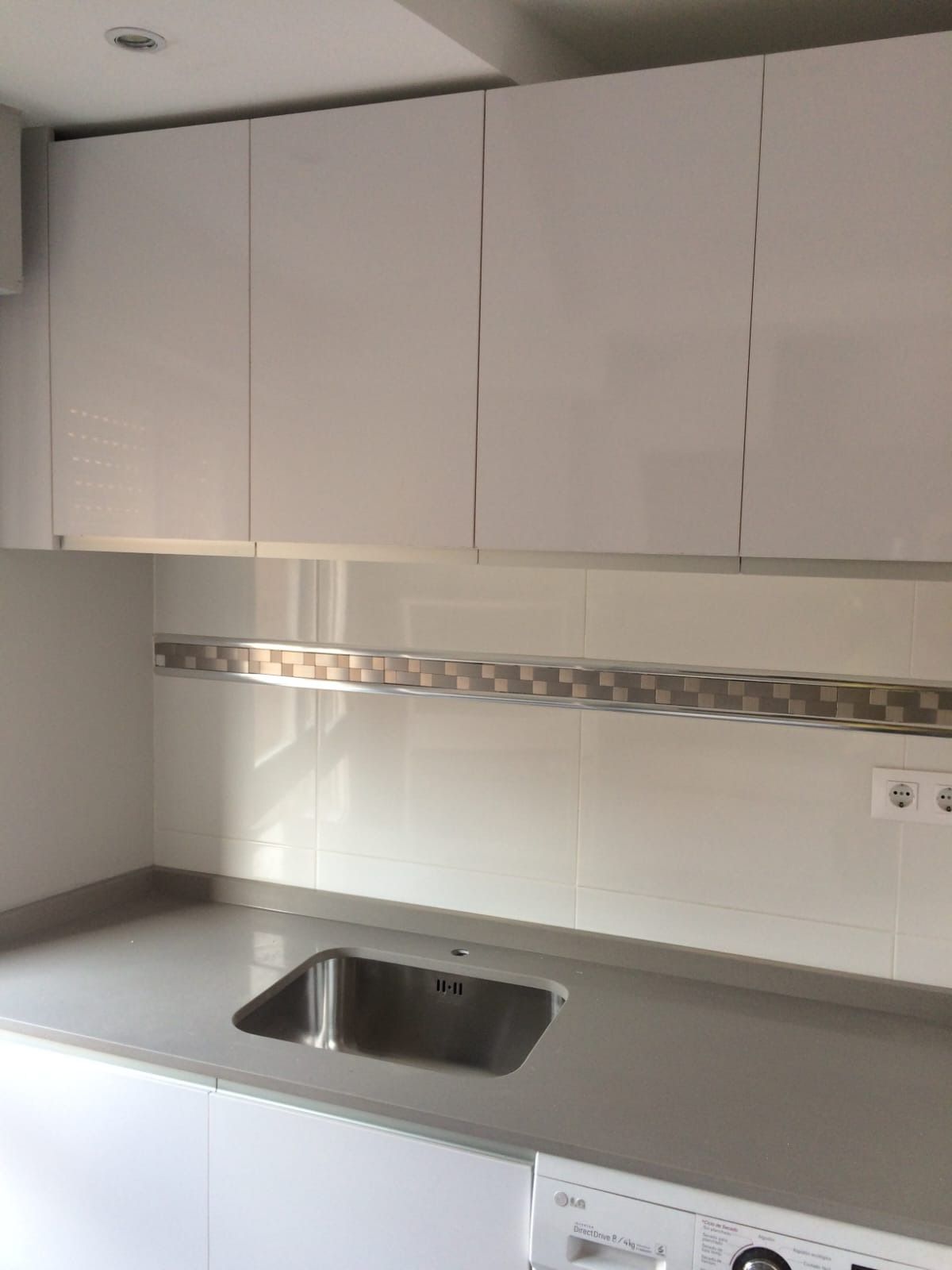 Una cocina moderna con armarios blancos brillantes sobre una encimera gris con fregadero integrado de acero inoxidable.