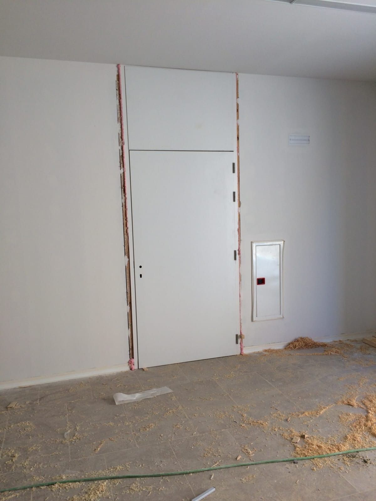 Una puerta blanca instalada en una pared interior sin terminar, con huecos visibles y aislamiento expuesto en los laterales.