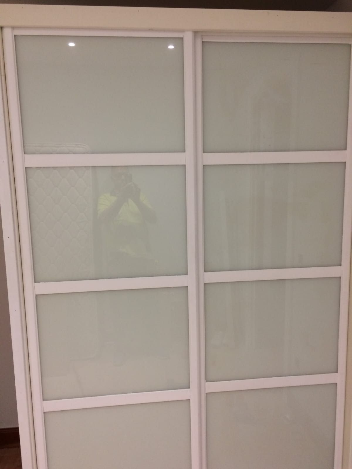 Un armario con marco blanco y puertas correderas con cuatro paneles de vidrio esmerilado cada una.