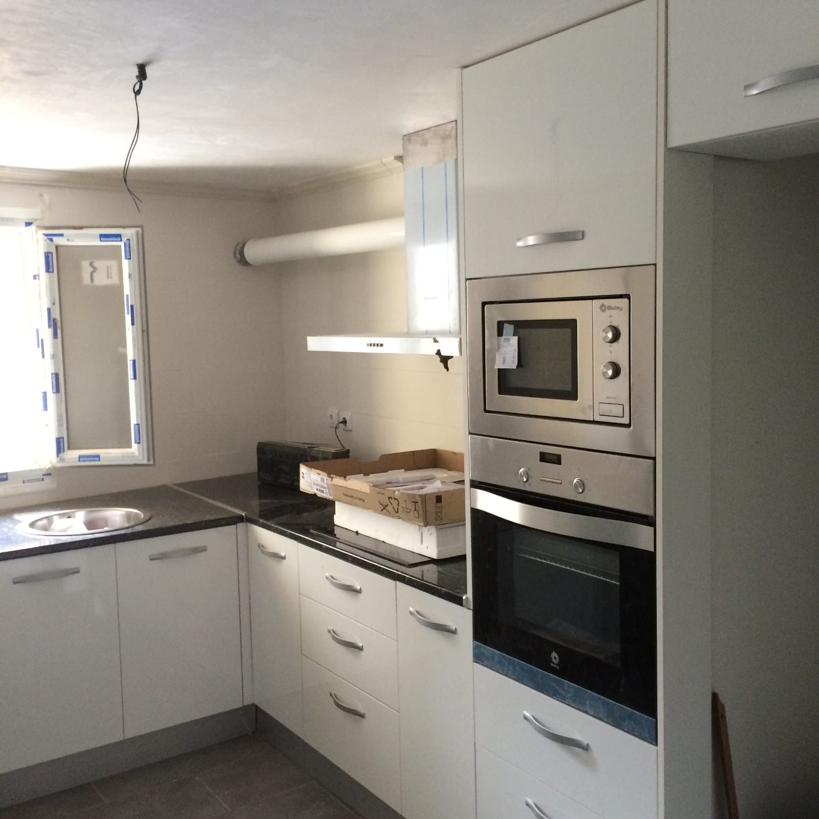 Una cocina moderna en proceso de renovación con gabinetes blancos, encimera negra y horno empotrado de acero inoxidable.