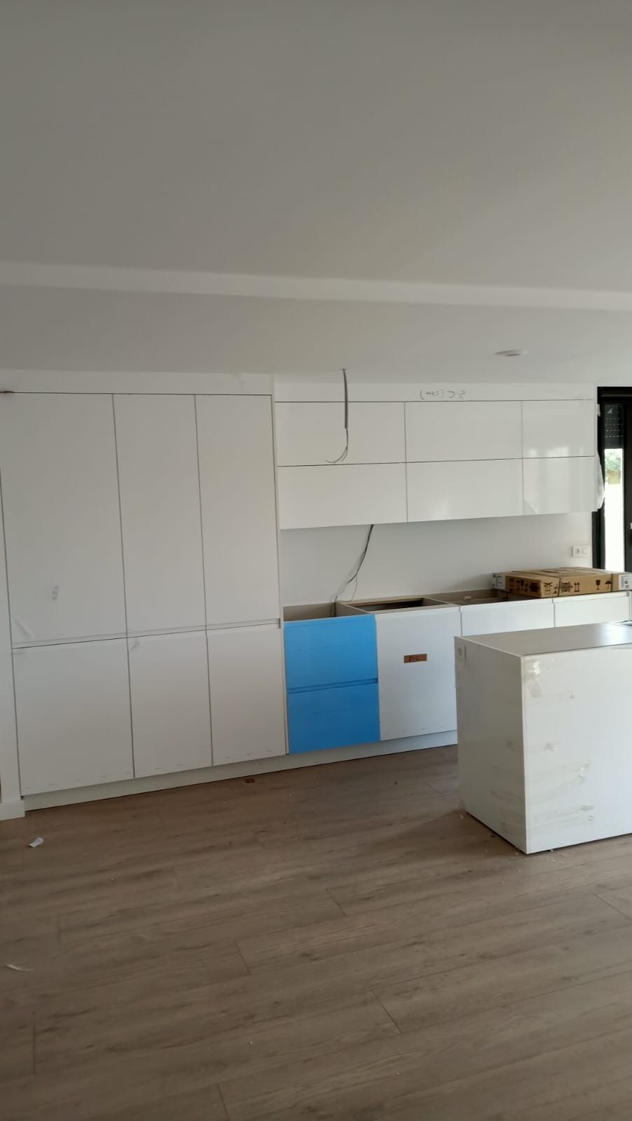 Una cocina moderna en construcción con gabinetes blancos, piso de madera clara y un gabinete inferior con ribete azul.