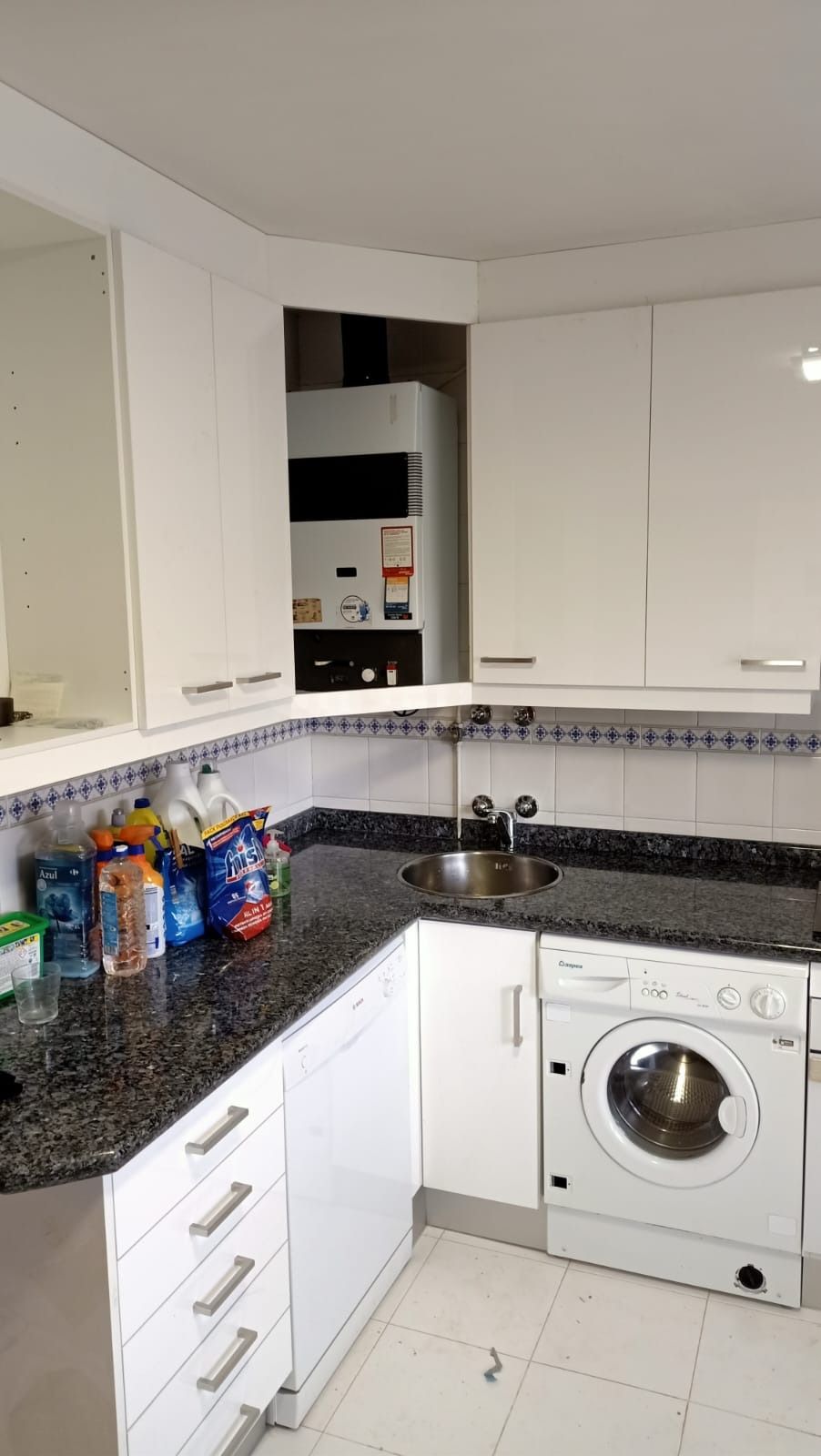 Un rincón de cocina moderno con armarios blancos, encimeras de granito oscuro, caldera integrada, fregadero y lavadora.