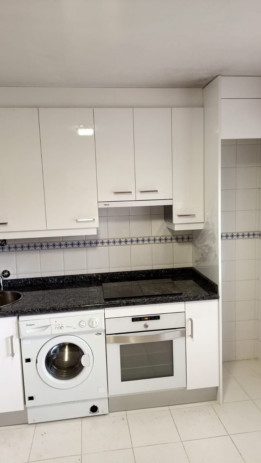 Una cocina blanca con elegantes armarios, encimera de granito, lavadora integrada y horno.