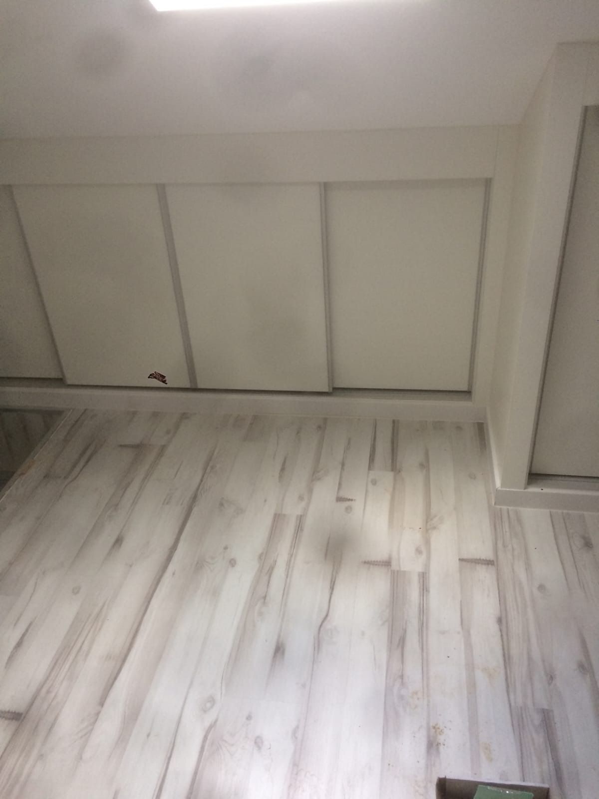 Una habitación con suelo de madera clara y armarios empotrados blancos a lo largo de la pared inclinada.