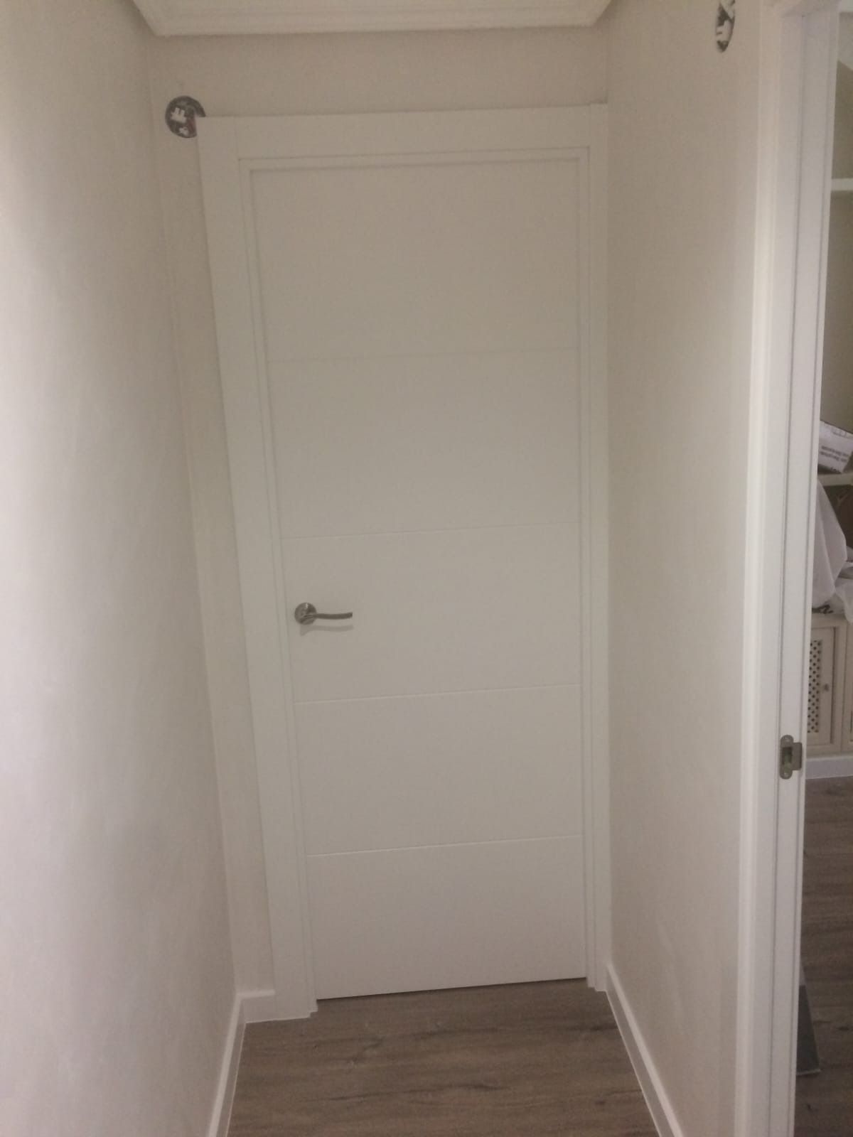 Una puerta interior blanca cerrada al final de un pasillo estrecho y de color claro con suelo de imitación madera.