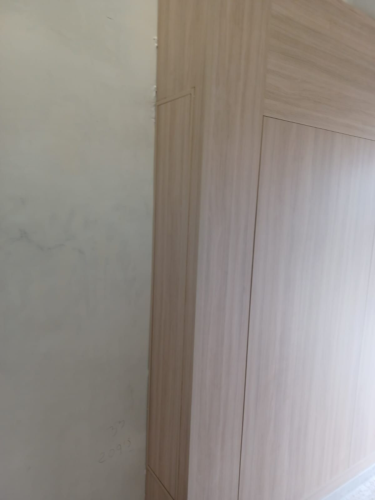 Vista de cerca de un panel de armario de madera clara que contrasta con una pared lisa de color claro con textura visible.