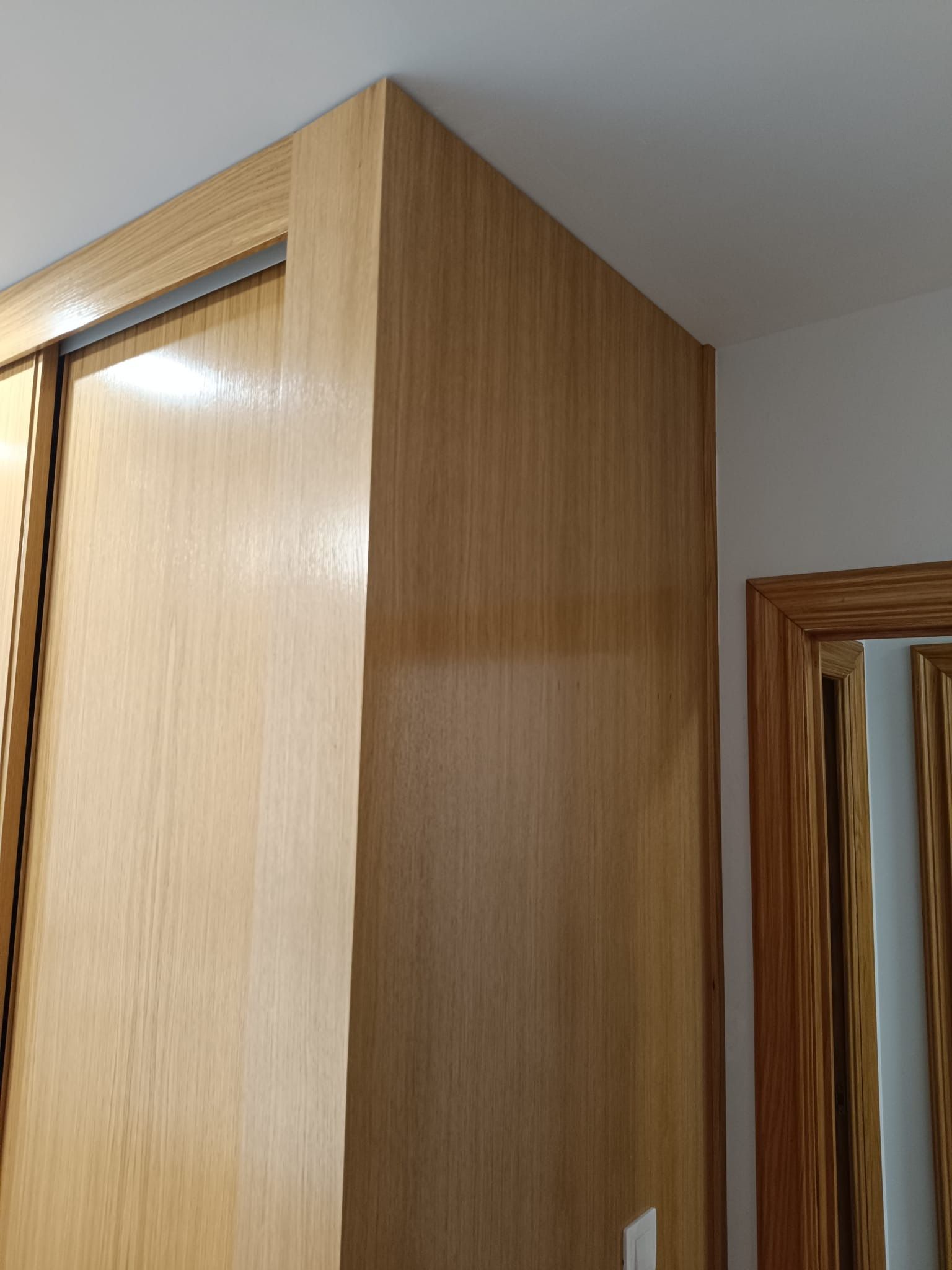 Un rincón de una habitación con un armario empotrado de madera clara y un marco de puerta a juego, sobre paredes blancas.