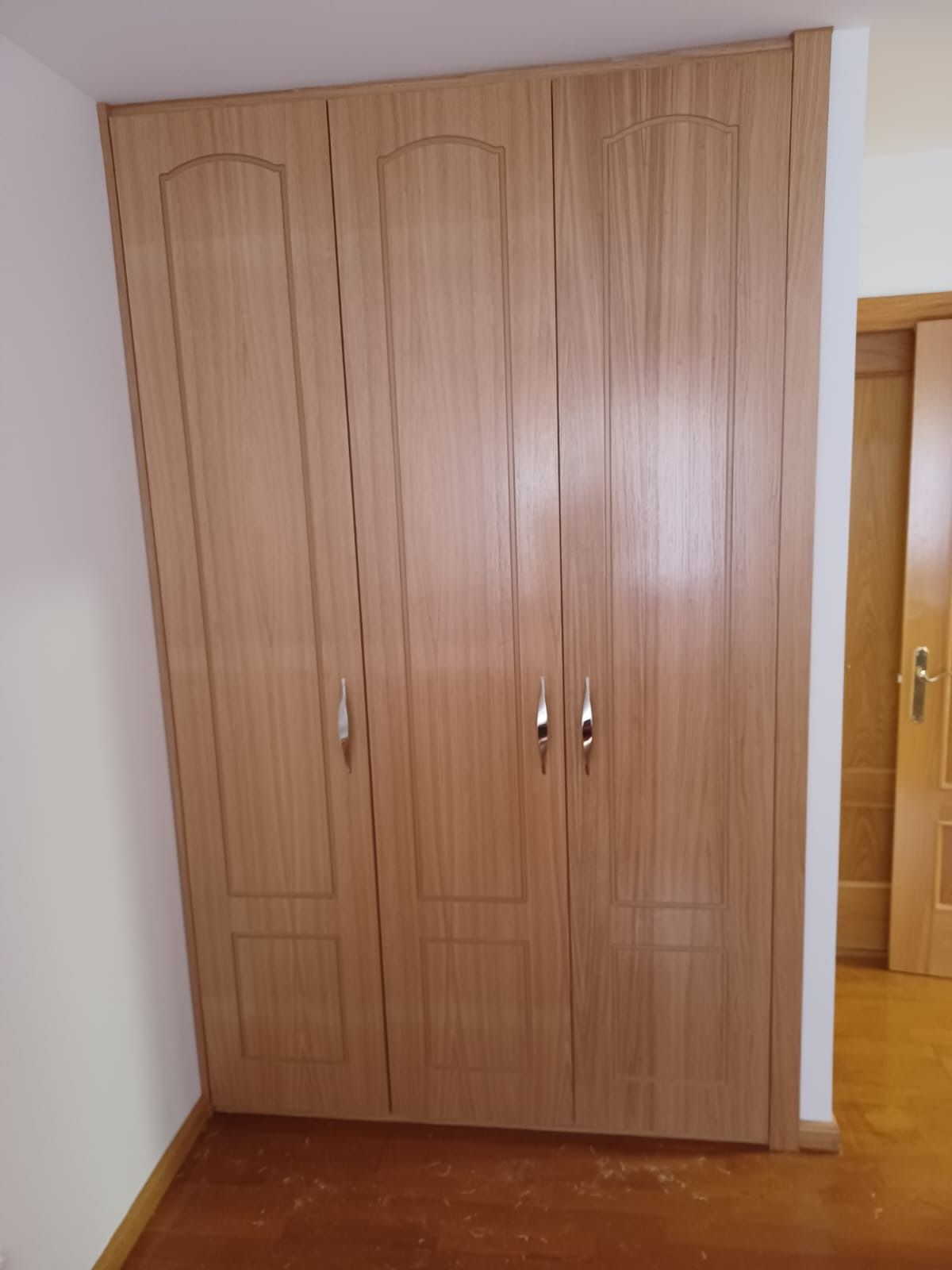 Un armario empotrado de madera de tres puertas con acabado de veta natural y tiradores plateados sobre una pared blanca.