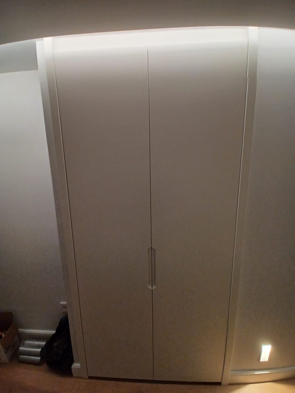 Armario blanco de dos puertas con tirador central vertical, situado contra la pared de una habitación.