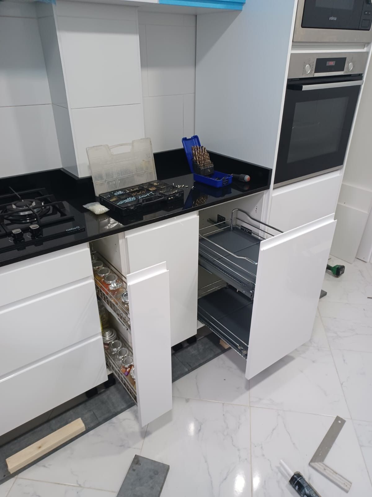 Cocina moderna en construcción con gabinetes blancos, encimeras oscuras y dos estantes con cajones extraíbles abiertos.