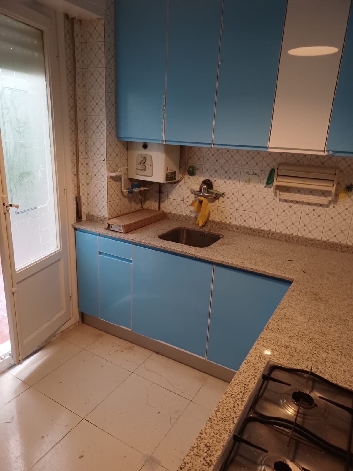 Una cocina de esquina con armarios azules, encimeras de granito moteado, fregadero de acero inoxidable y placa de gas.