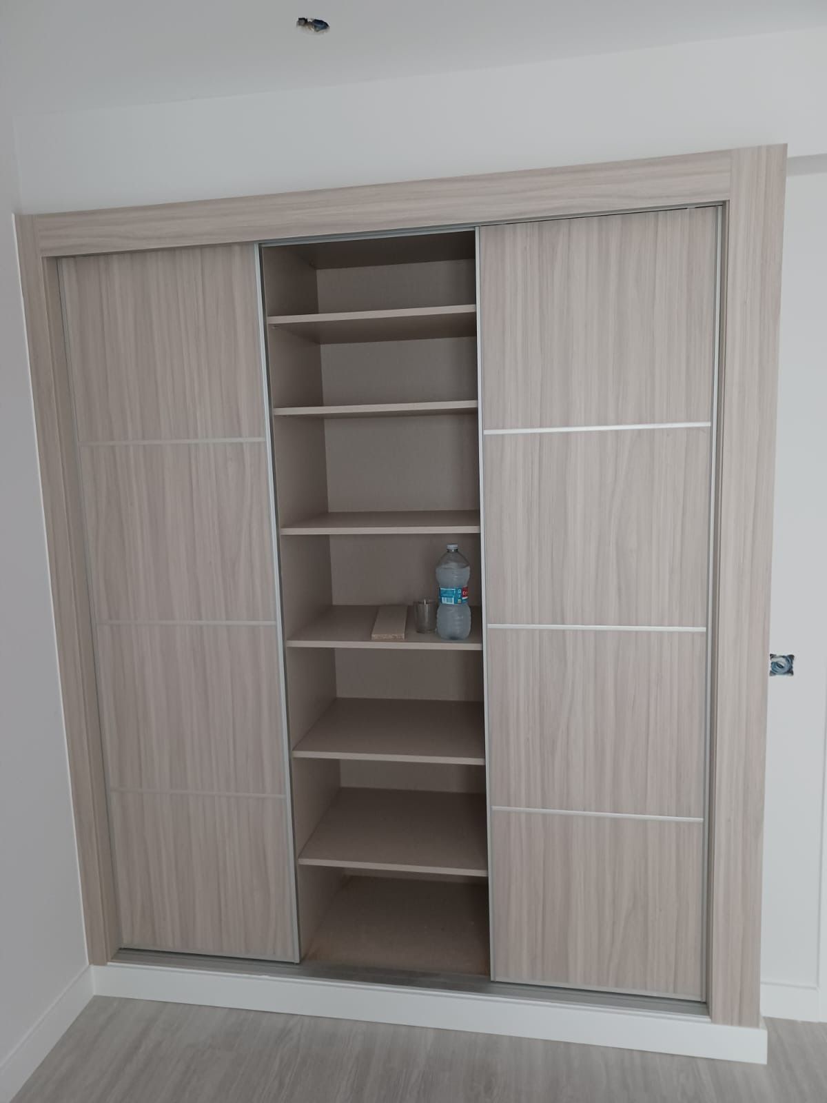 Un armario de madera clara con dos puertas correderas y una columna central abierta con siete estantes de almacenamiento.