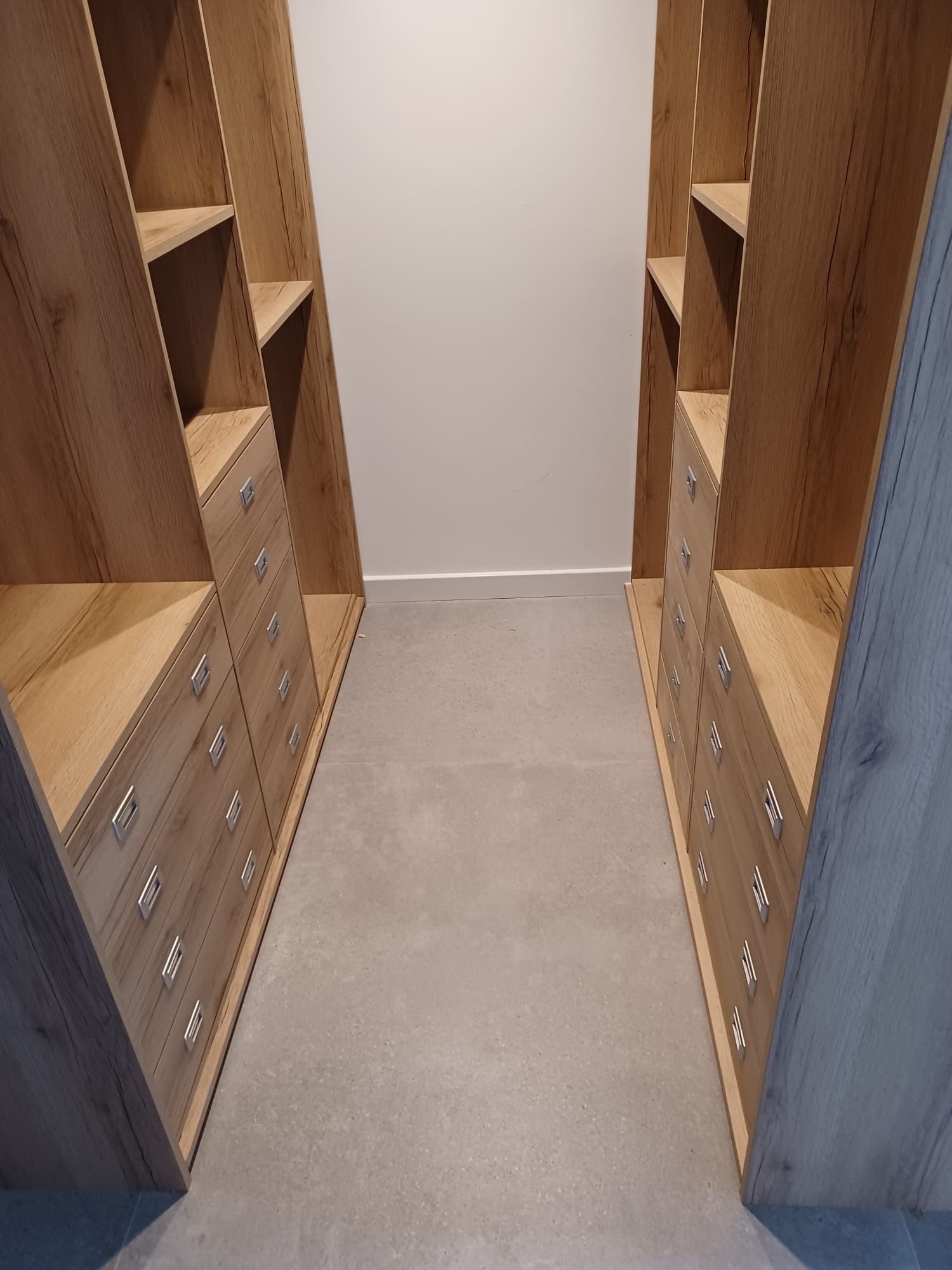 Un vestidor con dos estanterías a juego de madera clara y pilas de cajones que recubren ambas paredes laterales.