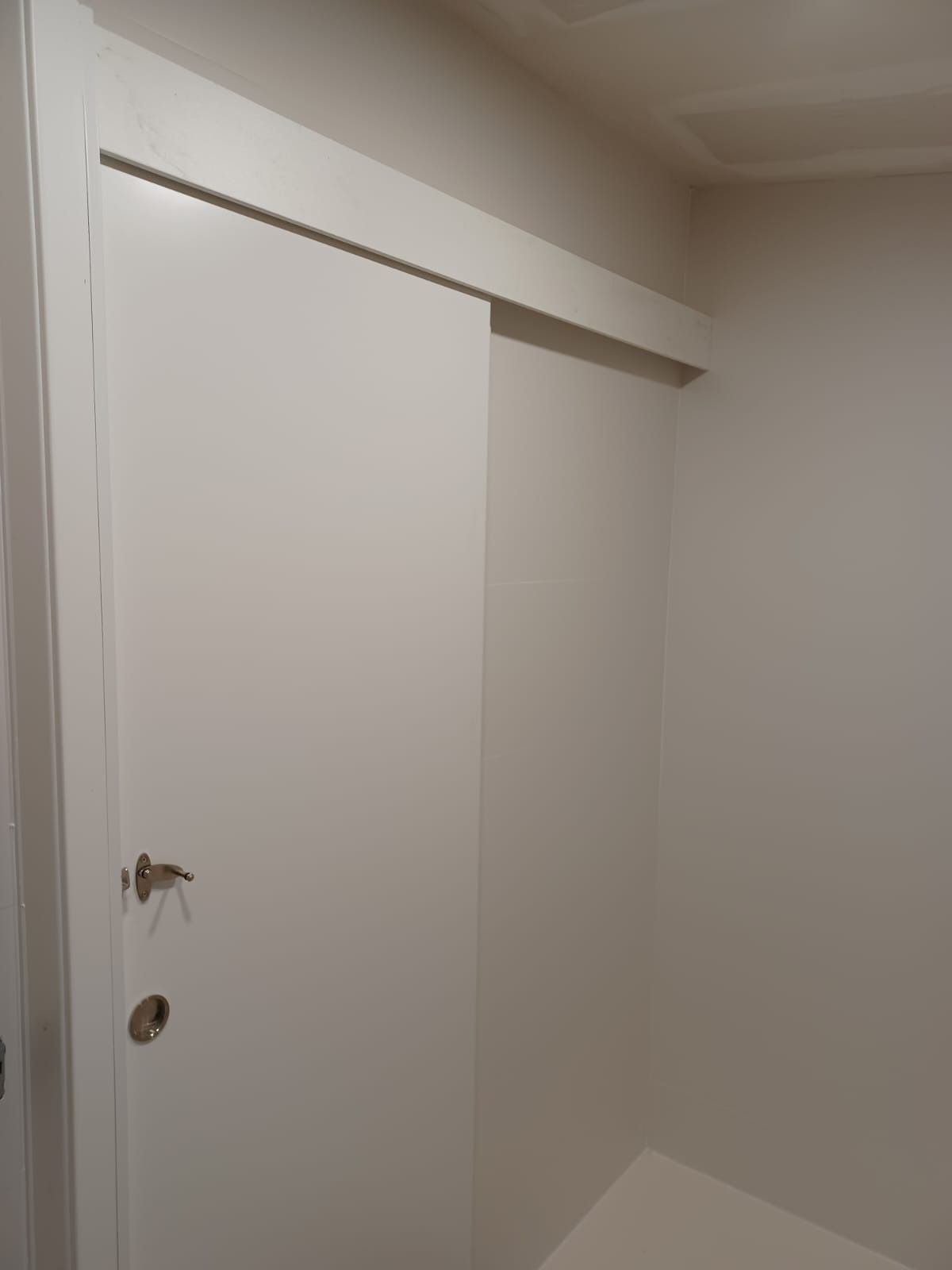 Una puerta corredera blanca estilo granero, montada sobre un riel, colocada contra una pared lisa de color claro.