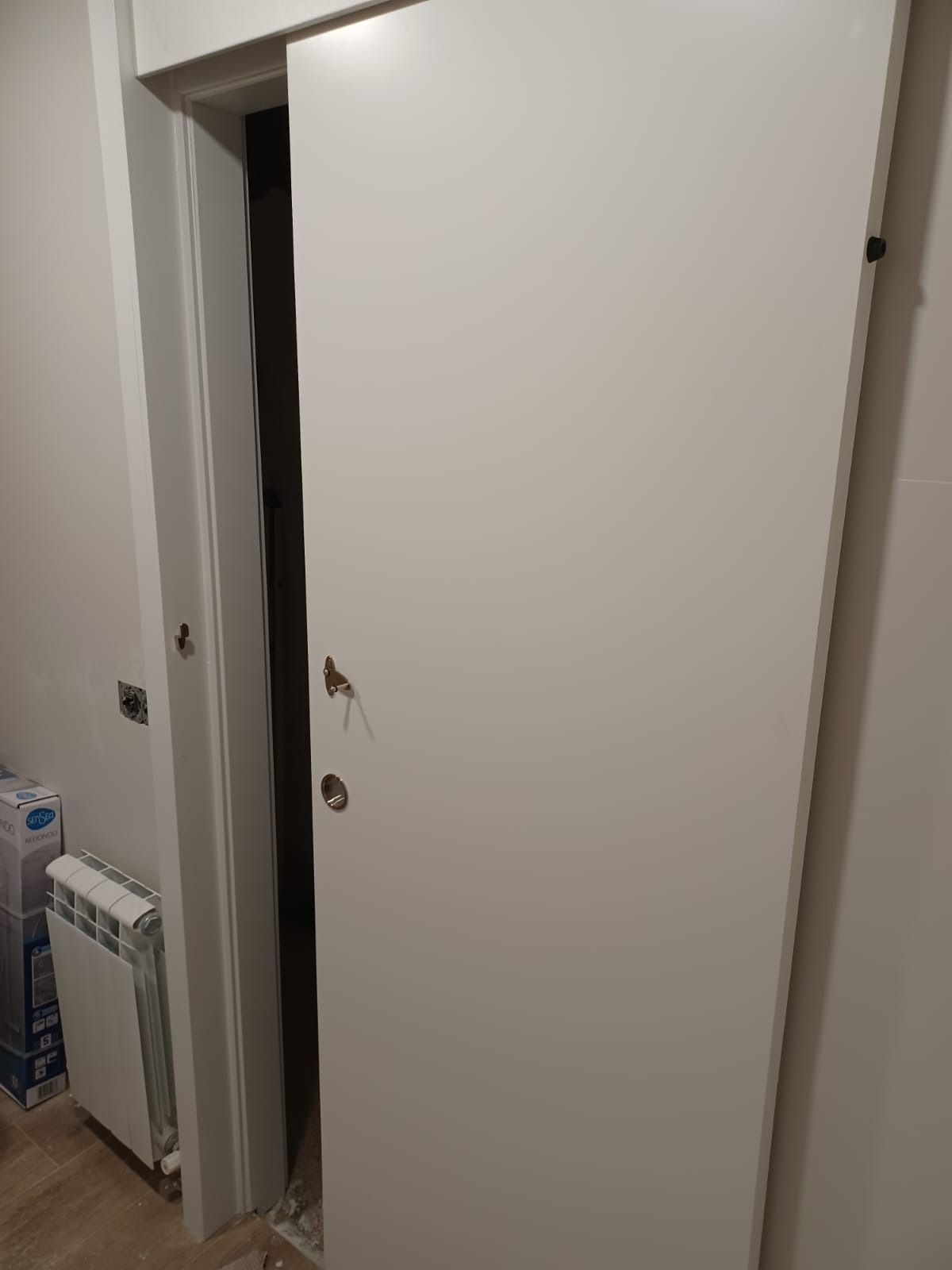 Una puerta corredera blanca entreabierta en una habitación con un calefactor blanco visible a la izquierda.
