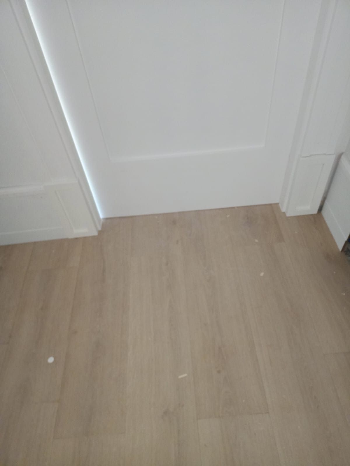 Una puerta y un marco blancos se alzan sobre un suelo de tonos claros que imita la madera.