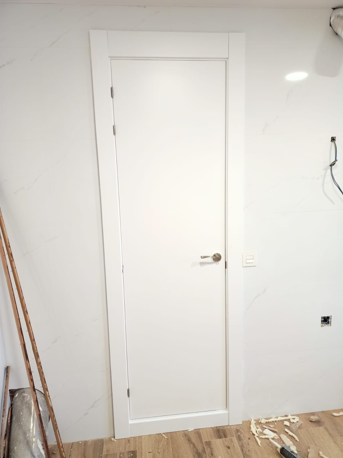 Una puerta interior blanca con tirador plateado instalada en una habitación con paredes blancas y suelo de madera sin tratar.