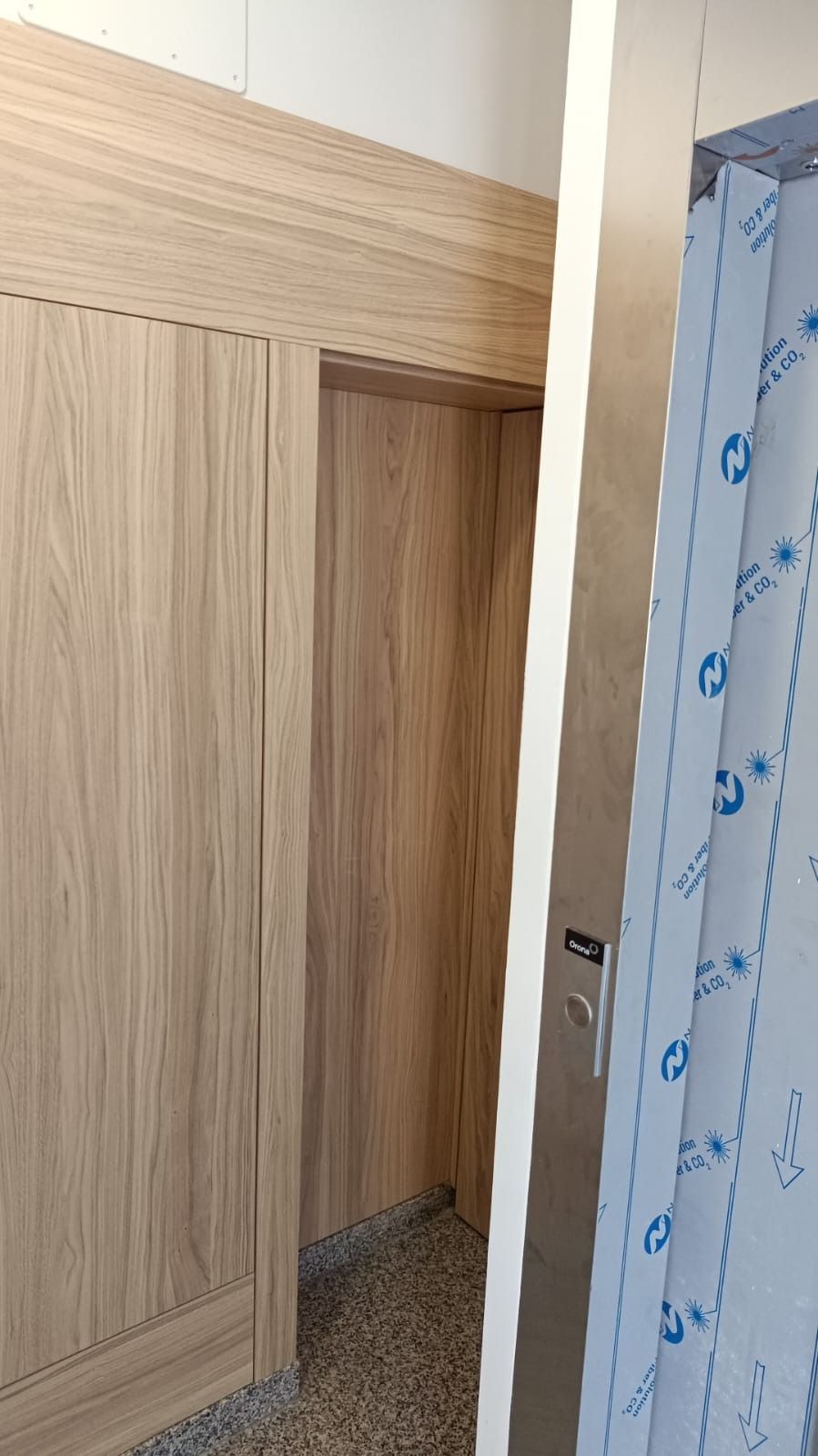 Una puerta con revestimiento de madera junto a un panel vertical cubierto con una película protectora azul.