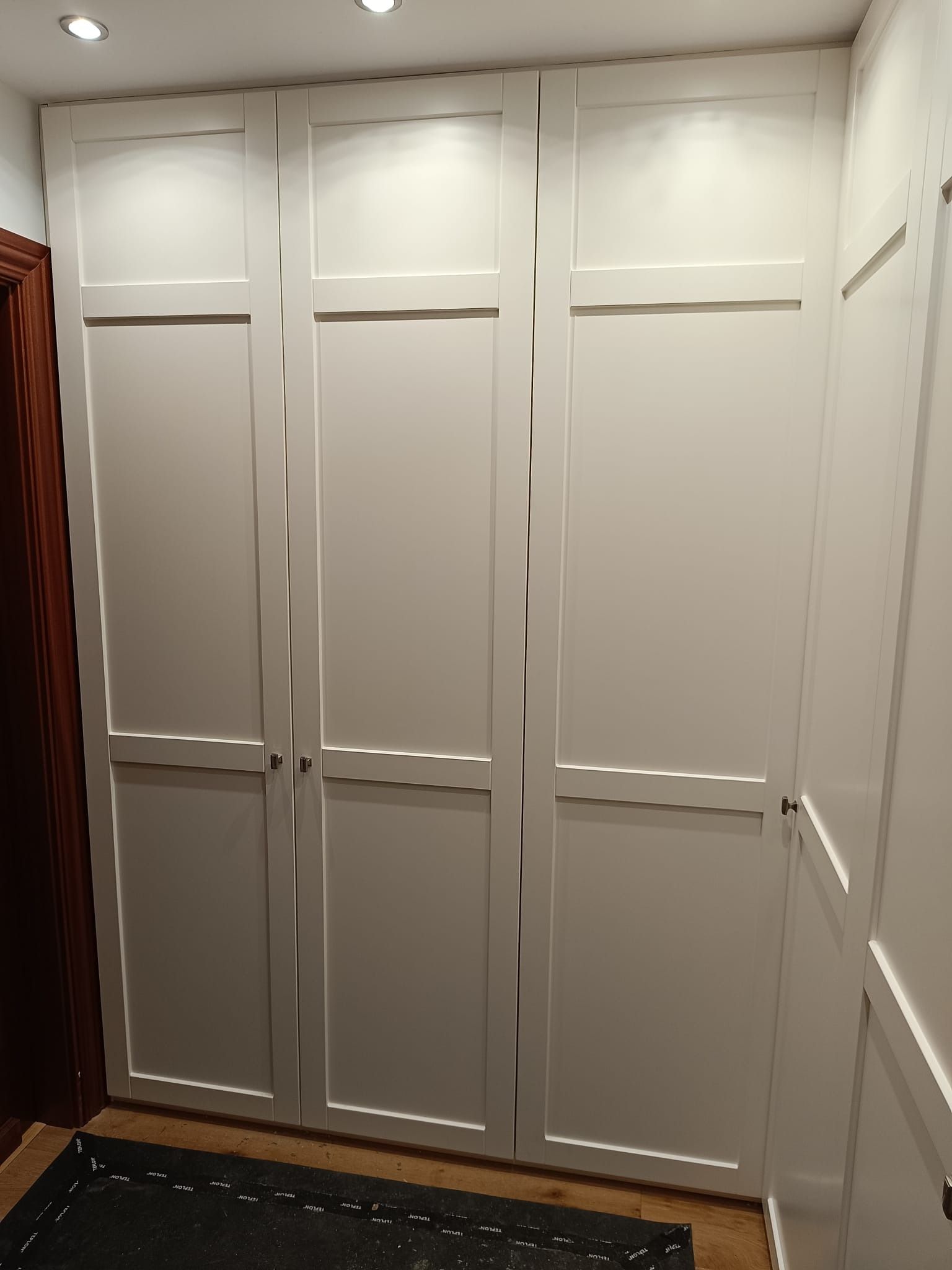 Un armario blanco de tres puertas que va desde el suelo hasta el techo, con un diseño clásico de paneles estilo Shaker.